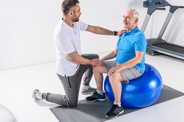 Rehabilitation Therapist Assisting Senior Man Exercising Fitness Ball Rehabilitation Therapist Assisting Senior Man Exercising Fitness Ball