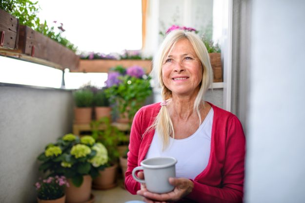 Senior woman with coffee on balcony in summer, relaxing among potted flowering plants. X Fun Date Night Ideas Near Your Senior Apartments In Marco Island, FL