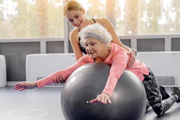 Smiling retiree leaning on fitball Cheerful grandmother