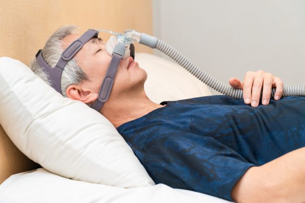 Middle age Asian man wearing CPAP headgear during his sleep Sleep Apnea In Your Loved Ones: How Senior Living Care In Marco Island, FL Can Help