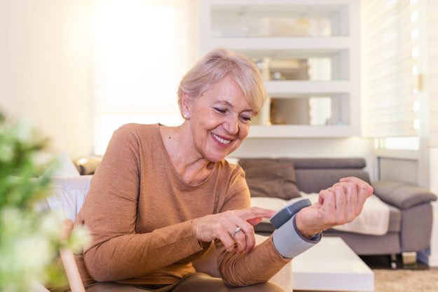Mature Woman Checking Blood Pressure. Close up view of a blood pressure monito on hand. Digital tonometr on human hand. Portrait of Senior woman measuring her blood pressure