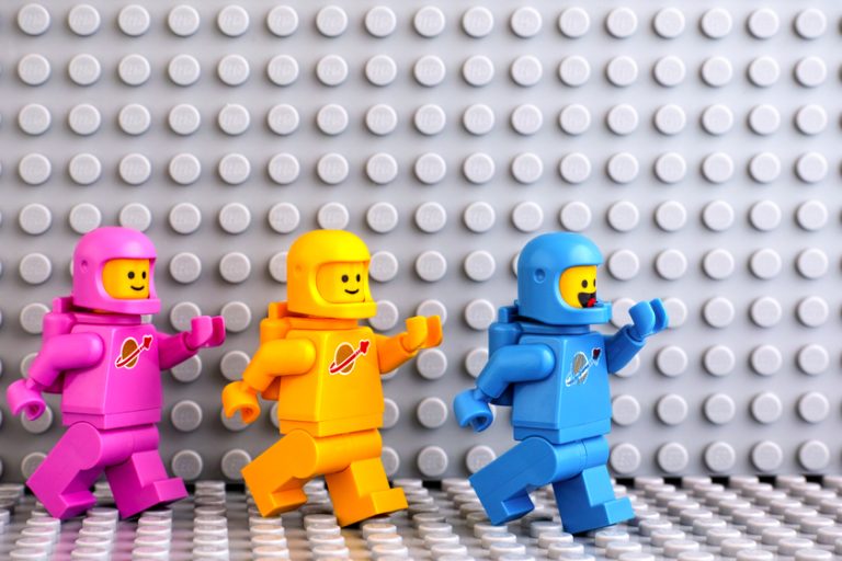 Three Lego astronaut minifigures going one after another on gray Three Lego astronaut minifigures going one after another on gray