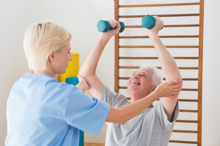 Senior man working out with his therapist in fitness studio