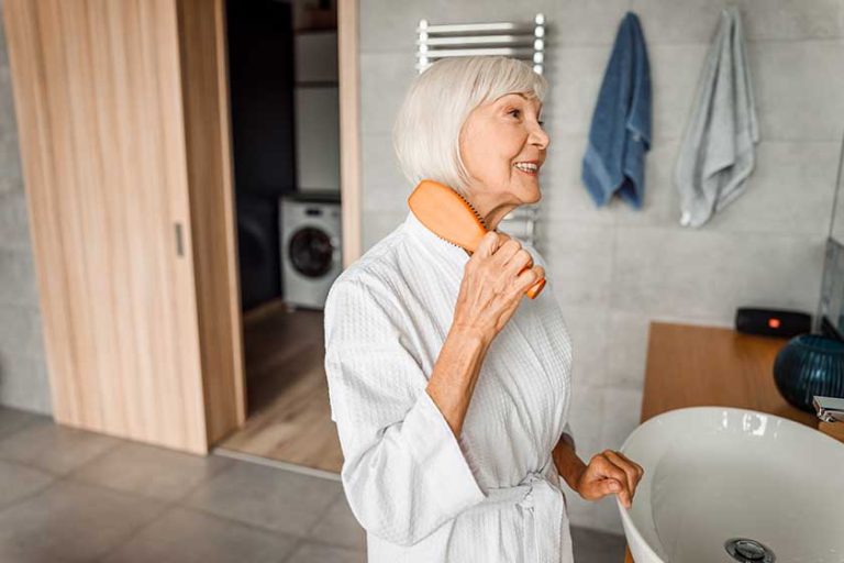 Cheerful old woman brushing hair and smiling