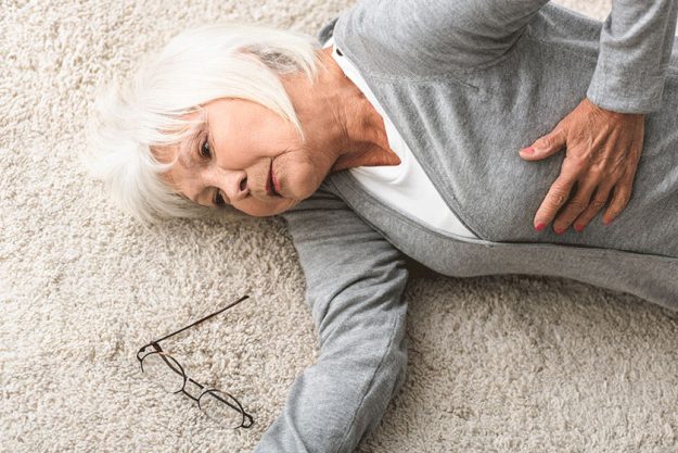Overhead view of sick senior woman lying on carpet