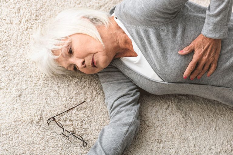 Overhead view of sick senior woman lying on carpet