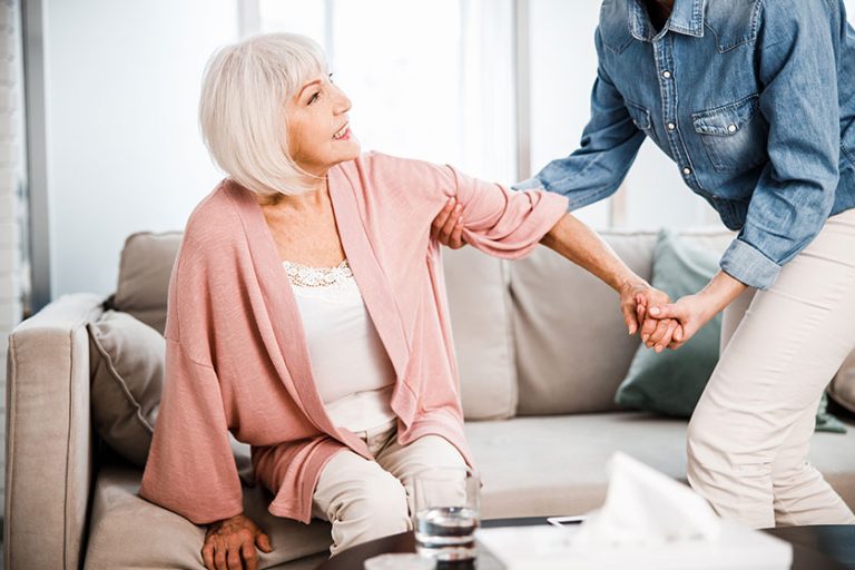 Young woman helping grandmother to get up off the couch Young woman helping grandmother to get up off the couch
