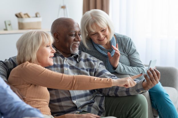 Cheerful elderly people spending time together at home, using smartphone Cheerful elderly people spending time together at home, using smartphone
