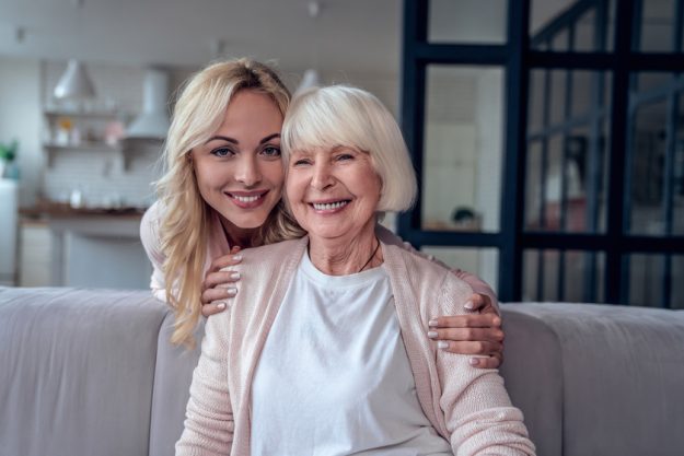 Senior woman and her attractive daughter spending time together at home and sitting on sofa. Happy Mothers' Day.