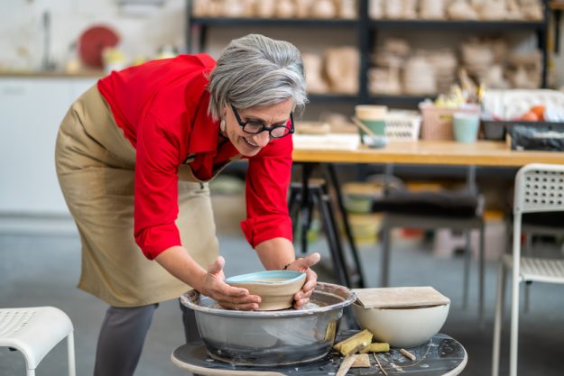 Woman potter taking finished plate from pottery wheel, making earthenware.