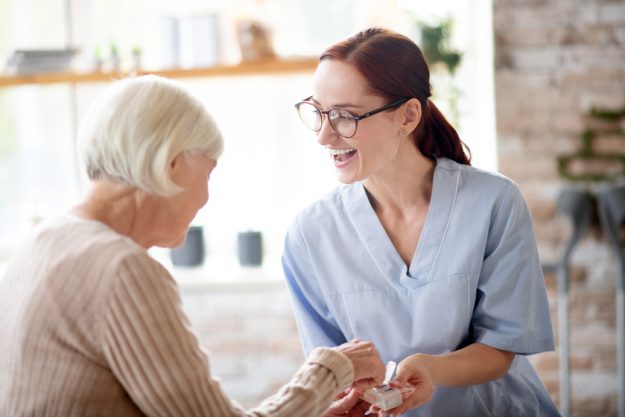 Pleasant nurse laughing while speaking with retired lady