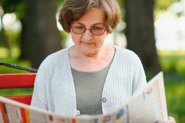 Adult woman sitting in park and reading newspapers Adult woman sitting in park and reading newspapers