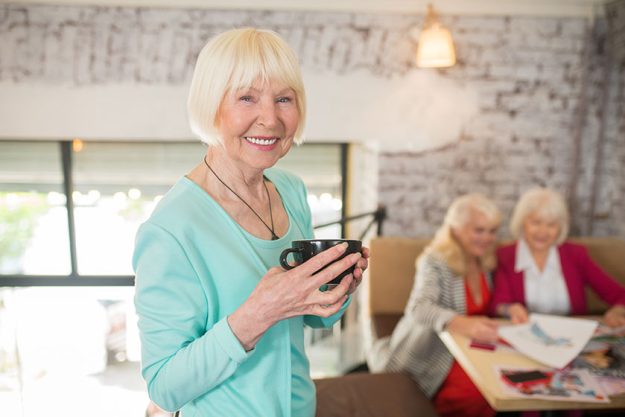 A blonde woman in a blue suit standing with a cup of tea in hands and smiling A blonde woman in a blue suit standing with a cup of tea in hands and smiling