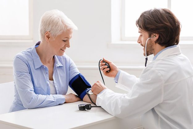 Doctor measuring blood pressure of senior woman at clinic