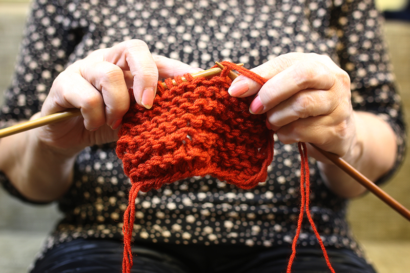 Elderly woman is engaged in knitting warm sweaters for her grand