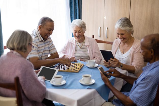 Senior friends playing chess and using technology