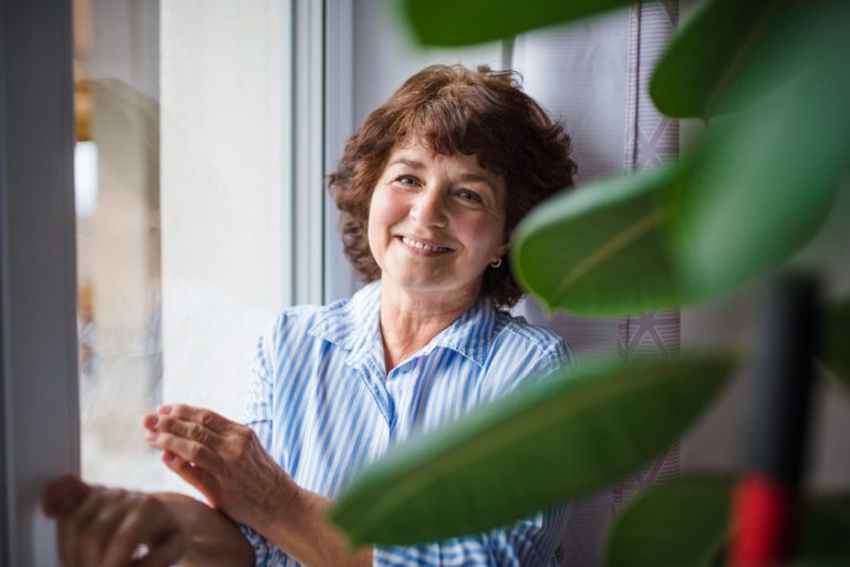 Senior woman standing by window at home, relaxing.
