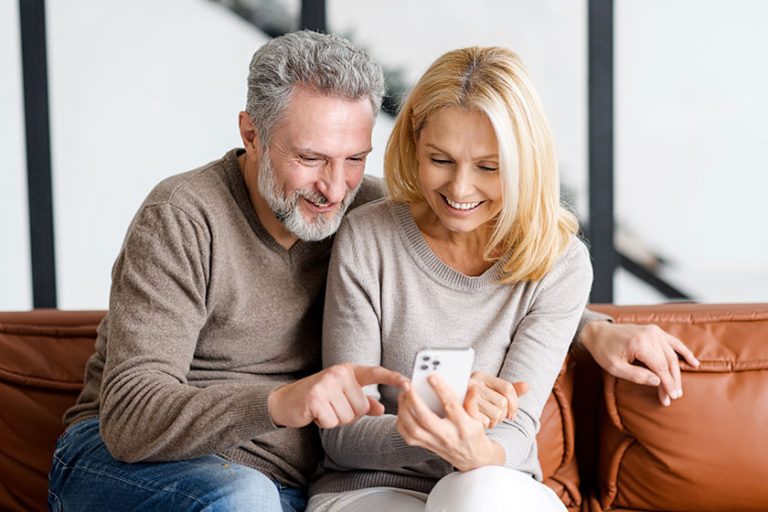 Happy senior couple with smartphone on the couch