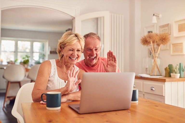 Retired Couple At Home In Kitchen Using Laptop