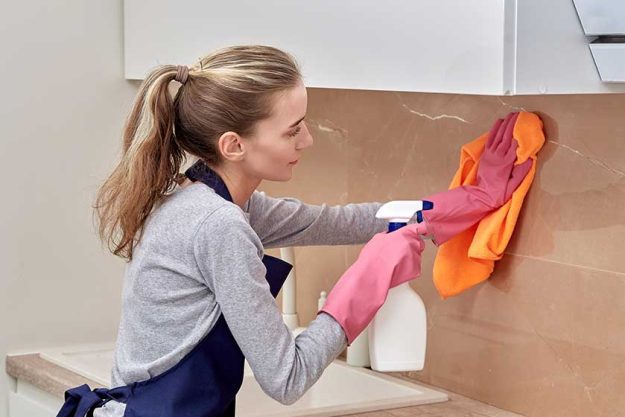 A young woman puts household chemicals on the wall in the kitchen A young woman puts household chemicals on the wall in the kitchen