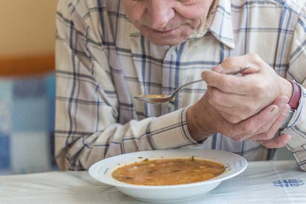 Elderly man with Parkinsons disease holds spoon in both hands