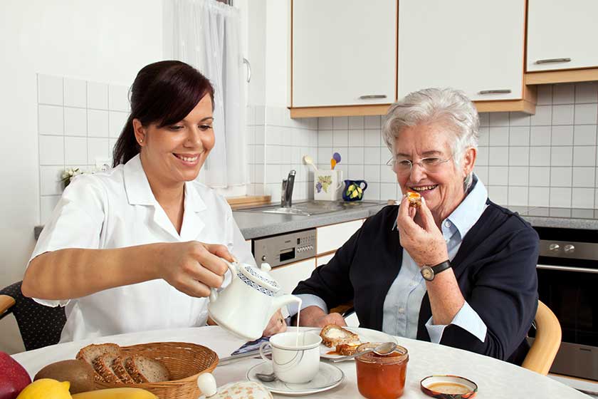 Nurse helps elderly woman at breakfast