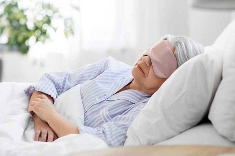 senior woman with eye mask sleeping in bed at home