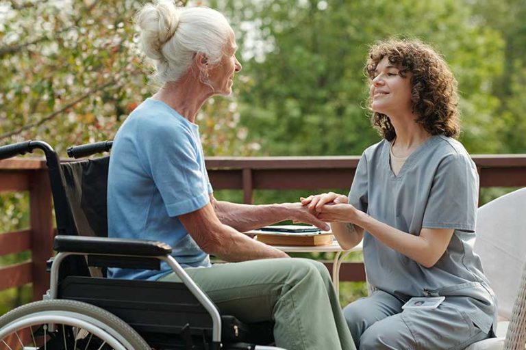 Young smiling caregiver uniform looking elderly woman disability sitting wheelchair