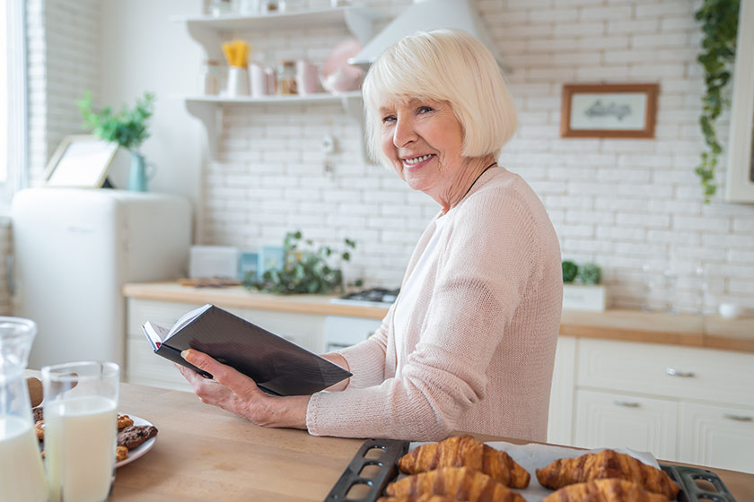 Attractive senior woman cooking on kitchen and reading recipe