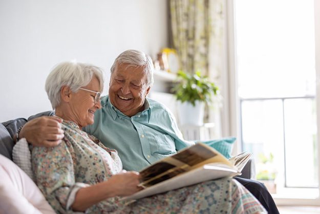 Elderly couple looking photo album while sitting sofa