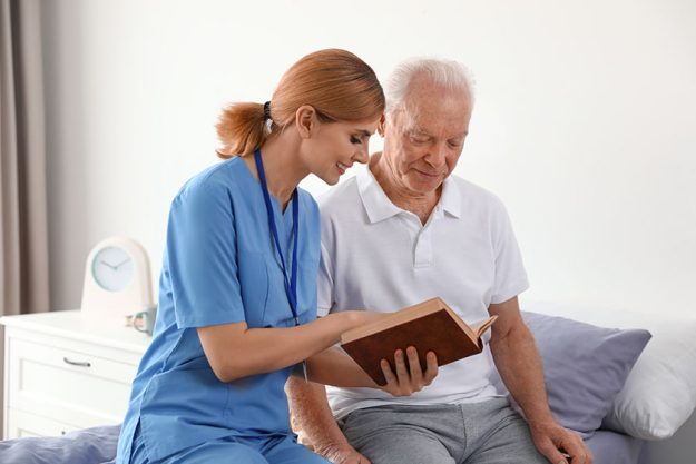 nurse reading book to elderly man indoors medical assistance nurse reading book to elderly man indoors medical assistance