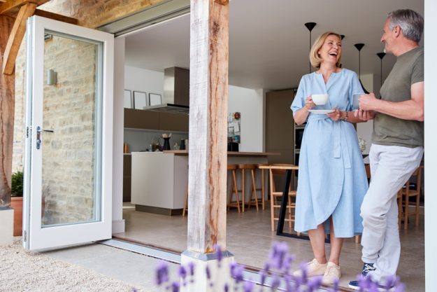 Senior Couple Standing And Looking Out Of Kitchen Door Drinking Coffee Senior Couple Standing And Looking Out Of Kitchen Door Drinking Coffee