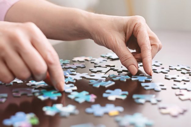 Elderly woman hands doing jigsaw puzzle closeup