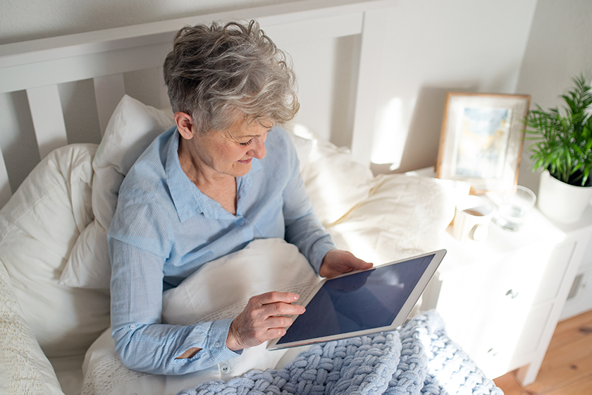 Happy senior woman using tablet in bed at home.