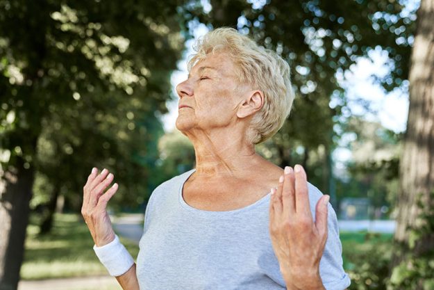 calm senior woman meditating park lake