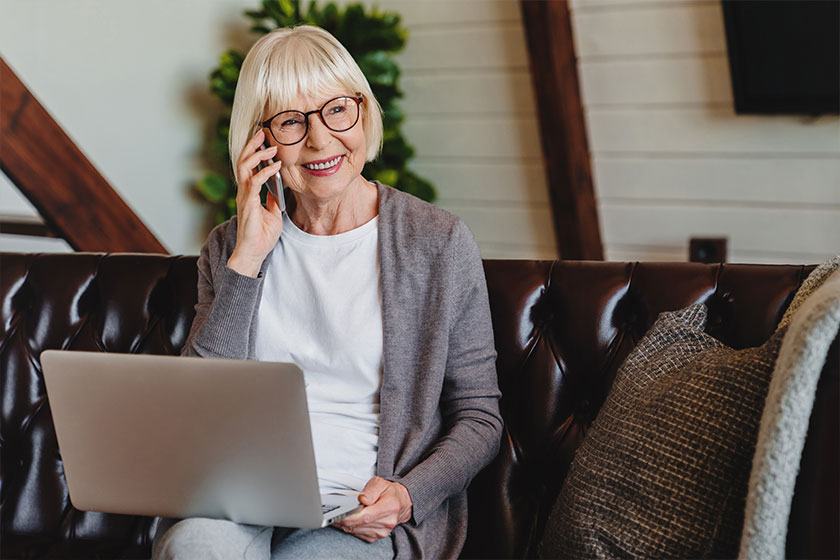 Mature woman talking mobile phone while using laptop
