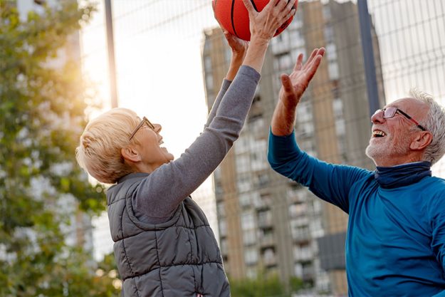 Senior woman and mature man playing basketball