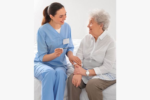 Young caregiver thermometer senior woman bedroom Young caregiver thermometer senior woman bedroom