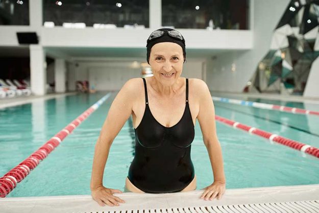 fit middle aged woman relaxing poolside swim cap goggles smile