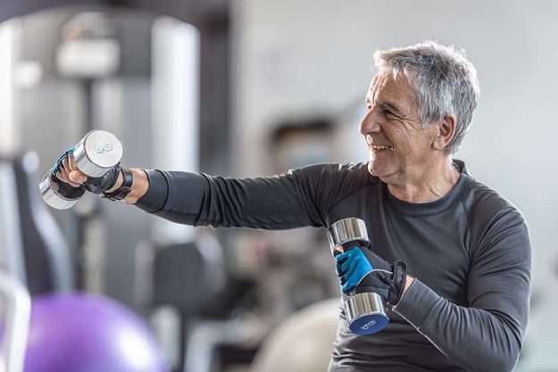 older man working out dumbbells gym smiling