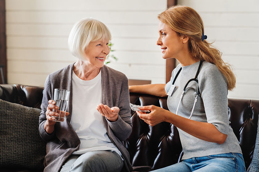 smiling nurse giving glass water medicines senior patient