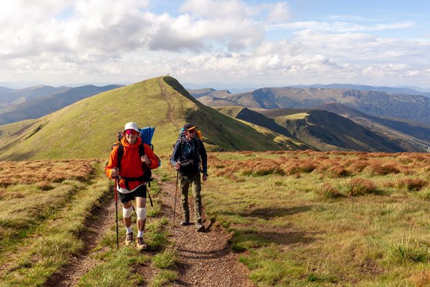 two men hiking equipment backpacks mountains trekking poles backdrop landscape
