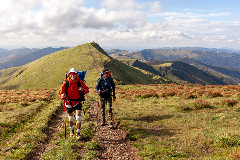 two men hiking equipment backpacks mountains trekking poles backdrop landscape