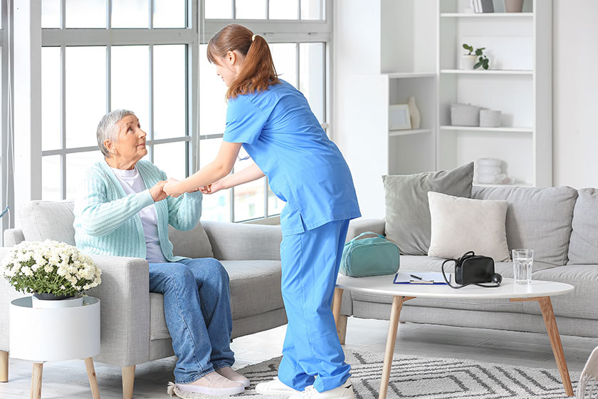 young caregiver helping senior woman stand home