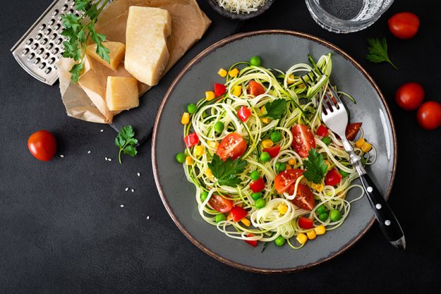 Zoodlie, healthy vegan food - zucchini noodlie with fresh green peas, tomato, bell pepper and corn for lunch, view from above
