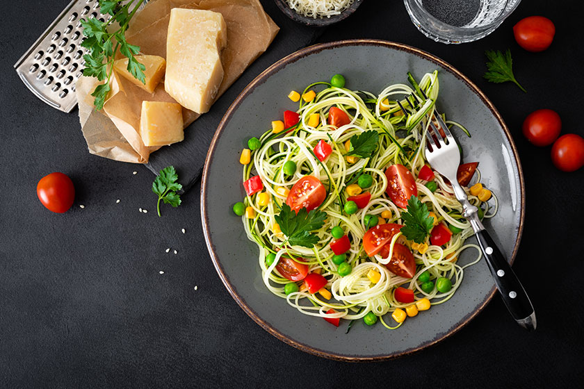 Zoodlie, healthy vegan food - zucchini noodlie with fresh green peas, tomato, bell pepper and corn for lunch, view from above