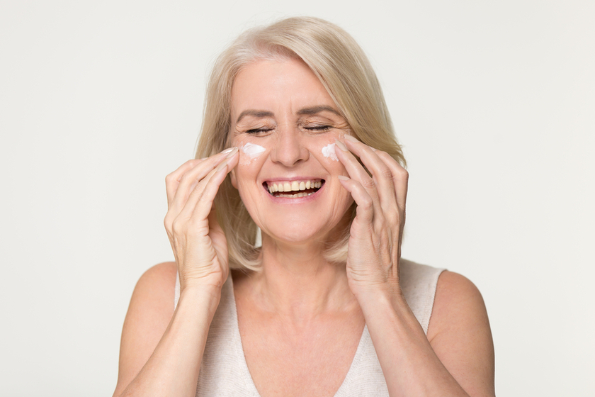 Happy old woman apply anti aging cream isolated on background