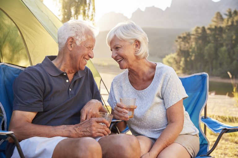 Senior Couple Enjoying Camping Vacation By Lake Making A Toast Senior Couple Enjoying Camping Vacation By Lake Making A Toast