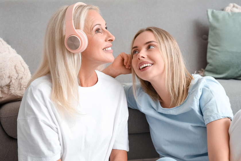 Happy young beautiful woman and her mother in headphones listening music at living room