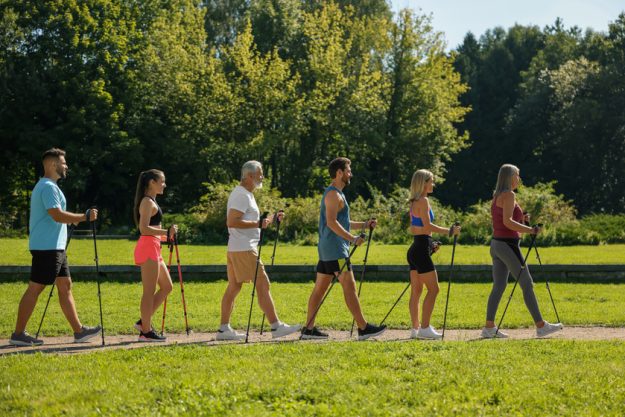 Group of people practicing Nordic walking with poles in park on Group of people practicing Nordic walking with poles in park on